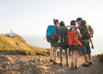 large family group wearing multi-day backpacks standing next to their beach campsite.