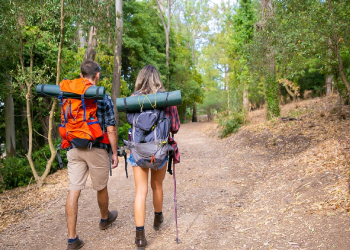 Two backpackers hiking along a wooded trail towards their campsite.