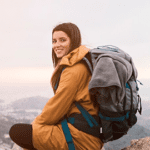 Woman backpacker sitting on a rugged mountain trail wearing fully loaded multi-day backpacking pack.