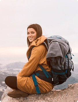 Woman backpacker sitting on a rugged mountain trail wearing fully loaded multi-day backpacking pack.