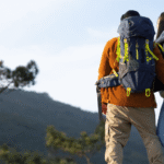 Two backpackers hiking up a rugged mountain trail wearing fully loaded multi-day backpacking packs.