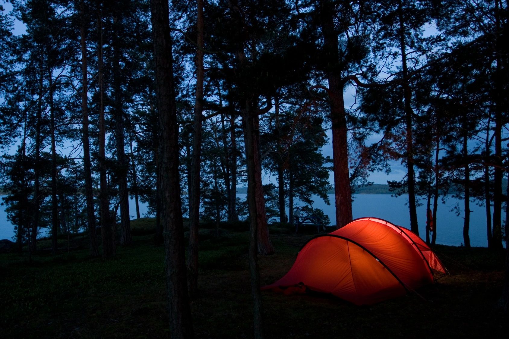 Two person camping tent illuminated beautifully in the night at a wooded campsite near a mountain lake.